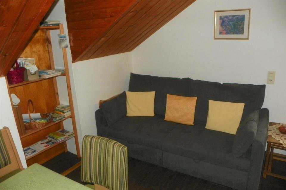 Ein anthrazitfarbenes Sofa mit drei gelben Kissen unter einer Dachschräge in der Ferienwohnung Eitner in Bad Weißenstadt. Zu sehen ist außerdem ein Holzregal.