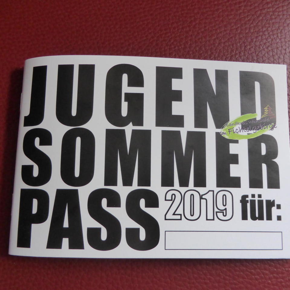 Ein Heft mit fetter schwarzer Schrift, auf der auf rotem Hintergrund „Jugend-Sommerpass 2019 für:“ steht. In der oberen rechten Ecke des Jugend-Sommerpass-Hefts befindet sich ein grüner Aufkleber mit unlesbarem Text.