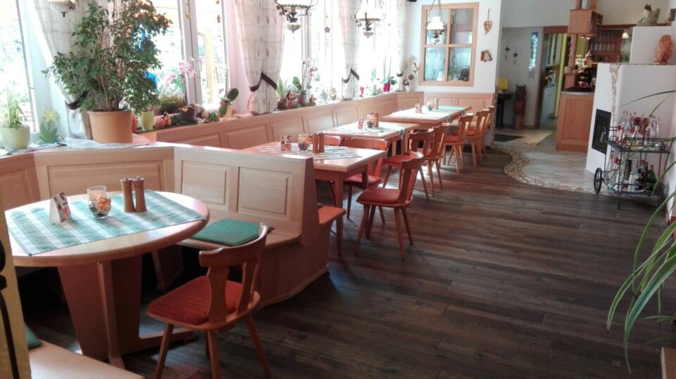 Das gemütliche Restaurant „Landgasthaus Birkenhof“ besticht durch Holzböden, Tische und Stühle mit grün karierten Tischdecken, während große Fenster für viel Tageslicht sorgen. Pflanzen schmücken die Fensterbänke und Tische und verleihen dem einladenden Raum eine frische Note. Das Restaurant wirkt leer.